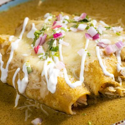 Enchiladas Verde topped with melted cheese, diced onion and drizzle of crema.