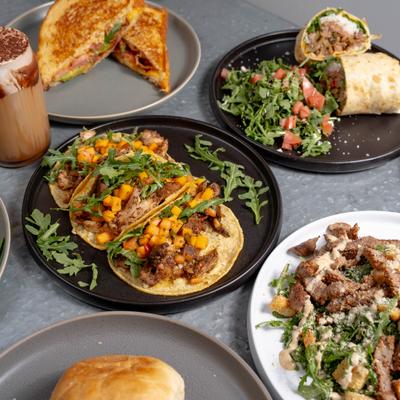 Plate of tacos served alongside sandwiches, salad, wrap and a drink.