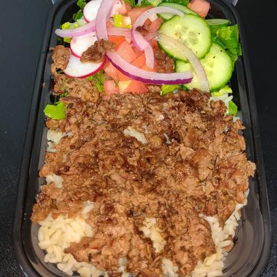 A black container with seasoned minced meat on rice, and a fresh vegetable salad.