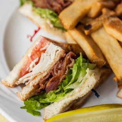 Turkey club sandwich with bacon, lettuce, tomato, and fries.
