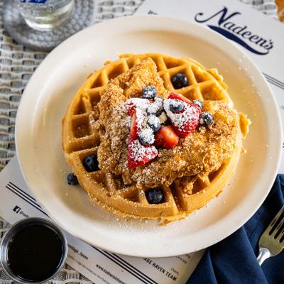 Chicken and waffles topped with berries and powdered sugar, served with syrup.