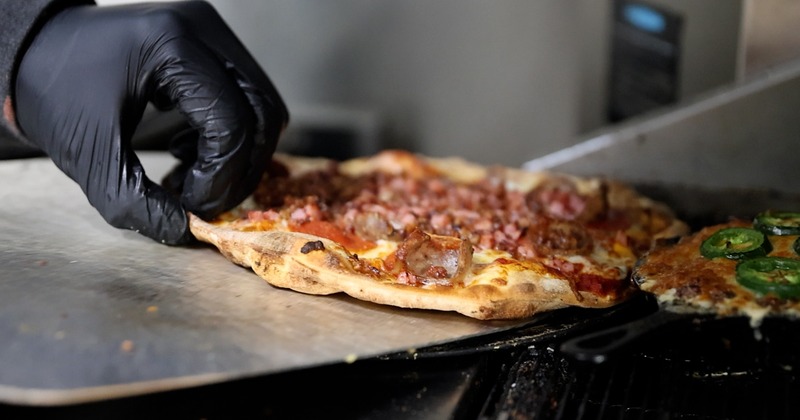 gloved hand pulling pizza topped with meat out of oven