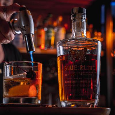 Old Fashioned drink being torched beside a bottle of bourbon.