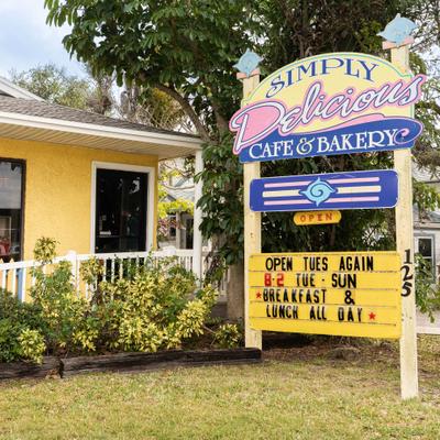 Simply Delicious Cafe and Bakery sign outside a yellow house building.