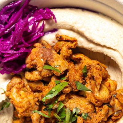 Hummus topped with chicken pieces, and purple pickled cabbage.