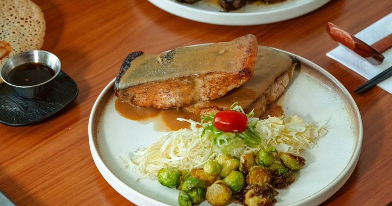 Seared salmon with sauce, Brussels sprouts, and slaw on a white plate