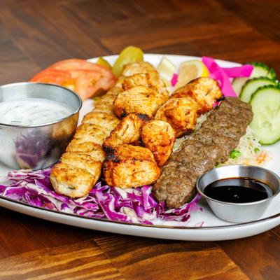 Mediterranean mixed grill platter with fresh vegetables and dipping sauces.