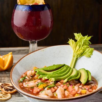 A bowl of ceviche with celery and avocado slices, accompanied with a red cocktail.