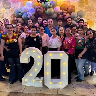 Group of people gathered for a celebration stanging behind large, illuminated number '20'.