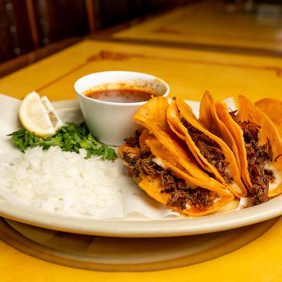Quesabirria tacos served with savory broth for dipping, chopped onion and cilantro.