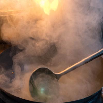 An employee stirring a content in a pot with steam rising from the surface.