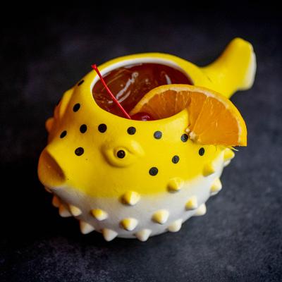Yellow pufferfish-shaped ceramic drink container filled with a liquid, garnished with a red cherry.