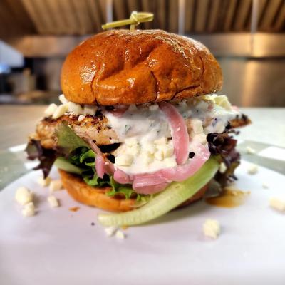 Grilled chicken sandwich with lettuce, pickled onions, and creamy sauce on a toasted bun.