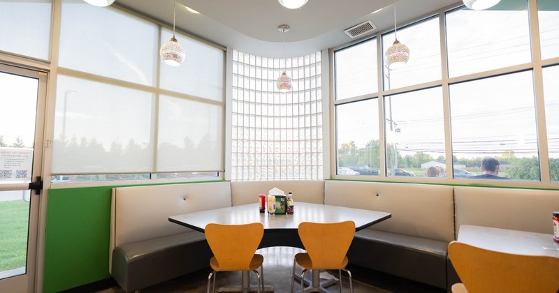 Bright booth area - large windows, globe pendant lights, a table with condiments, orange chairs.