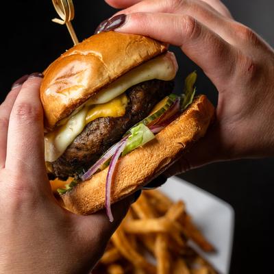 Hands holding a cheeseburger above fries.
