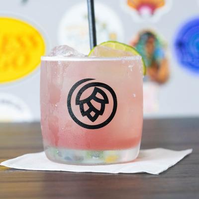 A light pink cocktail in a branded glass with a lime slice.