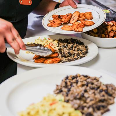 Person adding fried sweet plantains to a plate of food.
