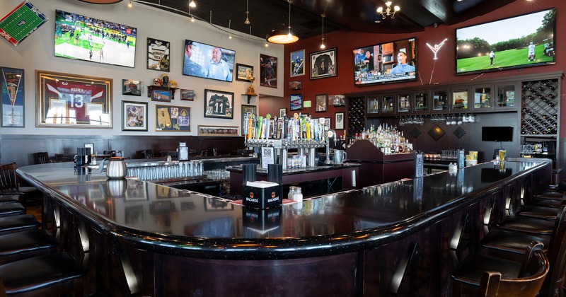 A spacious sports bar interior with a large U-shaped bar with black bar stools