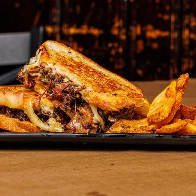A grilled sandwich with slow-braised beef and melted cheese, served with potatoes.