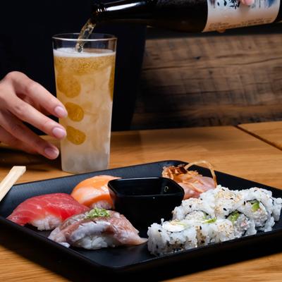 A person pours beer into a glass at a table with served sushi platter.