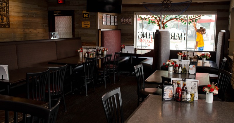 Interior of a restaurant with dark wooden tables, black chairs, and a long cushioned booth