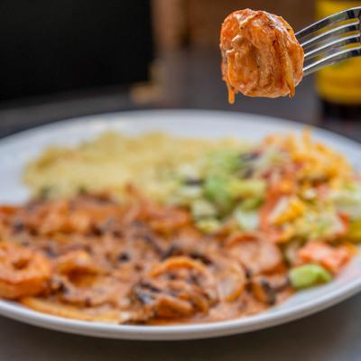 A fork holds a saucy shrimp in front of a plate with Camarones Chipotle dish.
