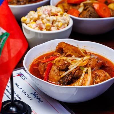 Bowl of chicken stew served alongside Haitian flag and other dishes.