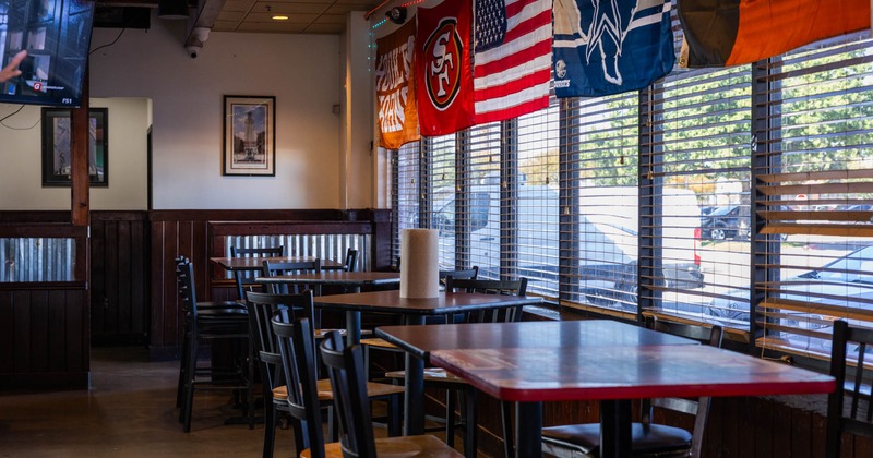 Interior, high seating tables with bar stools, windows with blinds, various flags hanged above