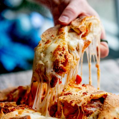 A person pulls apart a large chicken Parmesan clazone stretching the melted cheese.