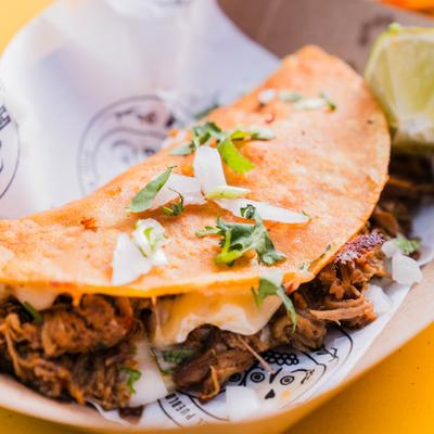 Birria taco topped with cilantro and diced onion, close-up.
