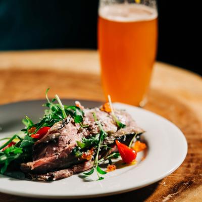 Steak salad with a glass of beer on a wooden table.