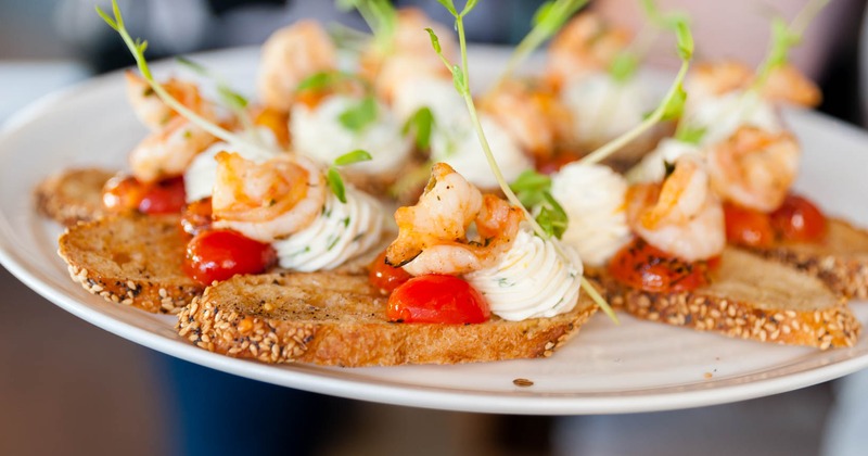 Sesame crostini slices topped with prawn, cream and cherry tomato, close up