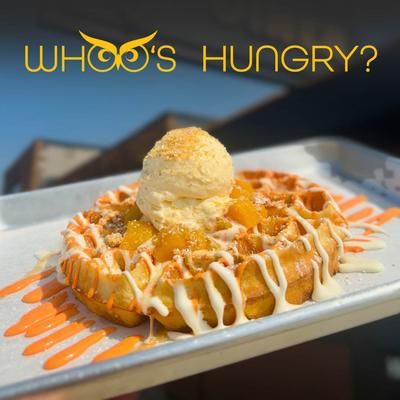 Waffle topped with peaches, ice cream, crumble, and  white and orange drizzle.
