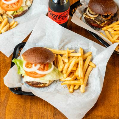 Various burgers served on the table with fries and a bottle of soda.