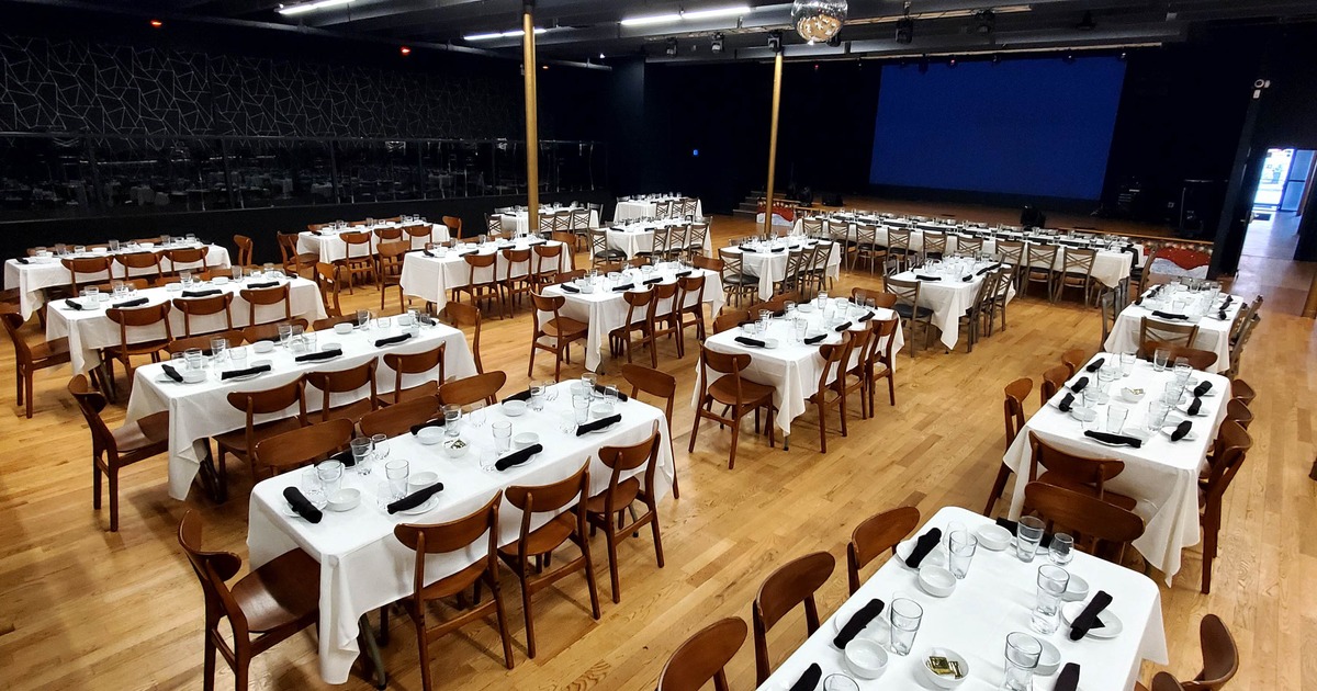 Banquet hall set up with multiple rectangular tables covered in white tablecloths