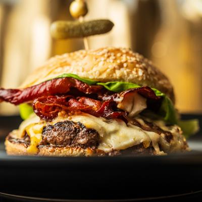 Bacon cheeseburger on a sesame seed bun topped with a pickle.