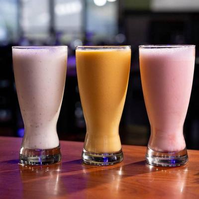 Sweet lassi, mango lassi, and strawberry lassi on a wooden counter.