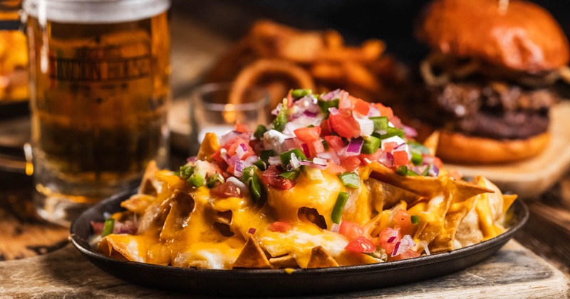 Loaded Nachos,  A burger, fries, and a pint of beer are in the background