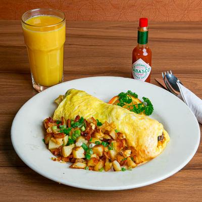 Omelet and breakfast potatoes, served with hot sauce and a glass of orange juice.