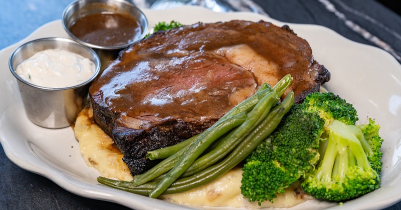 Prime rib topped with gravy, served with mashed potatoes, broccoli and green beans