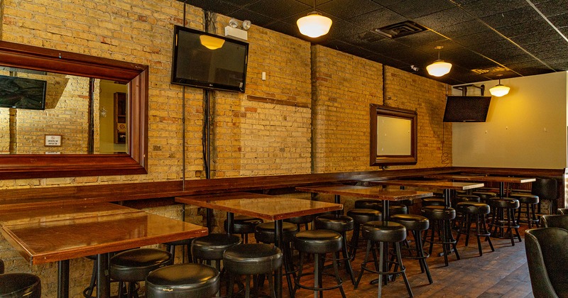 Interior, lined up tables with bar stools, brick wall with TVs and framed mirrors
