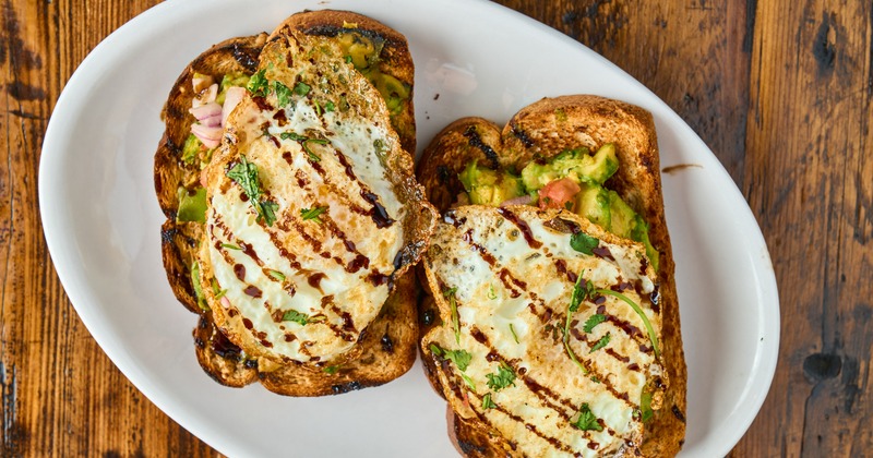 Two pieces of avocado toast topped with fries eggs