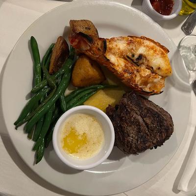 Grilled lobster tail with green beans, roasted potatoes, and steak, accompanied by melted butter.