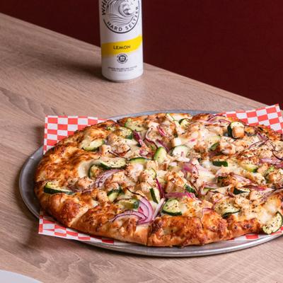 Vegetable and chicken pizza on a metal tray with a can of lemon hard seltzer.