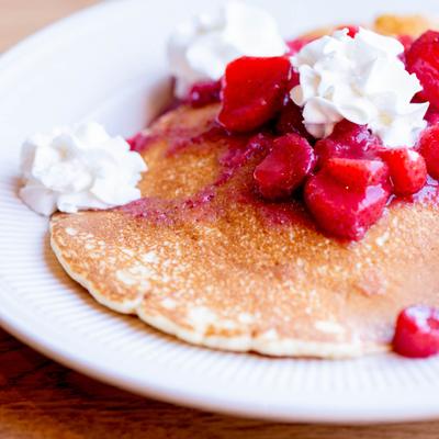 Plate of pancakes topped with strawberries and whipped cream.