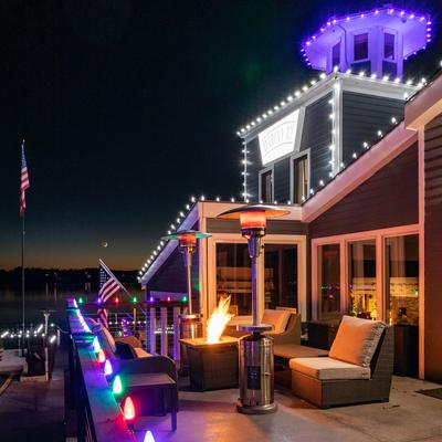 Outdoor deck at night, fire pit, patio furniture, and a building with decorative lighting.