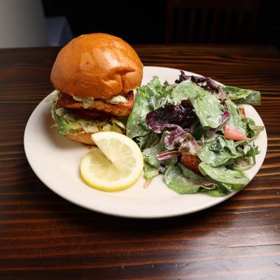 Grilled Salmon on a Brioche Bun and house salad lemon wedge.