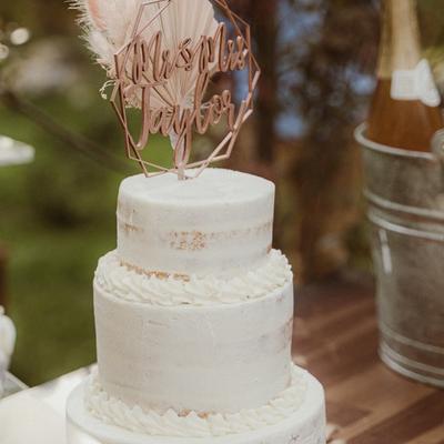 White wedding cake topped with a decorative sign, nearby, a sparkling wine bucket.