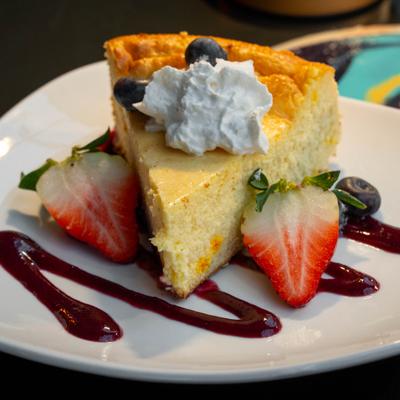 Cheesecake slice with berries, whipped cream, and berry sauce on plate.