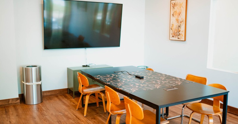 A modern meeting room with a dark table and a large wall mounter TV